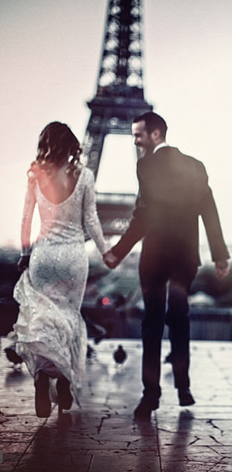 Couple holding hands near Eiffel Tower at sunset.