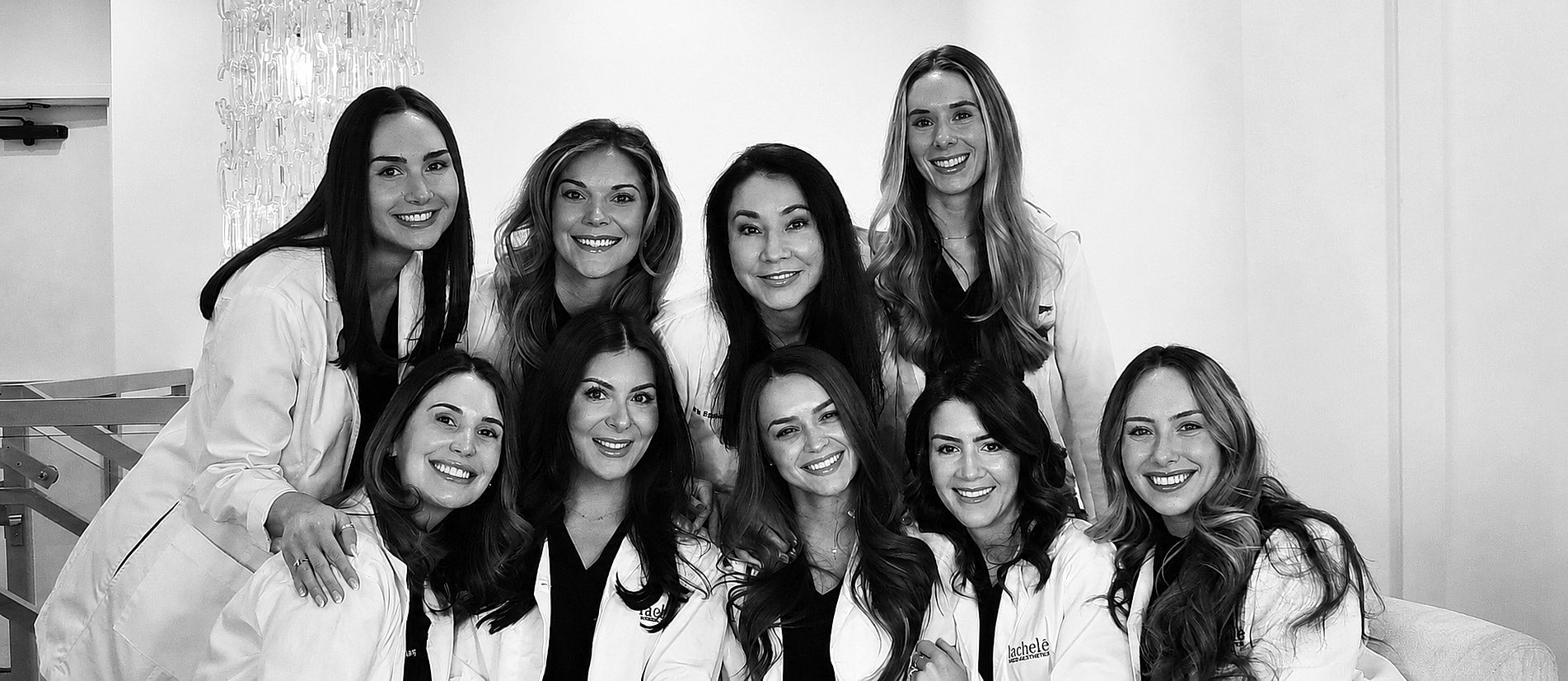 Group of women wearing white lab coats, smiling.