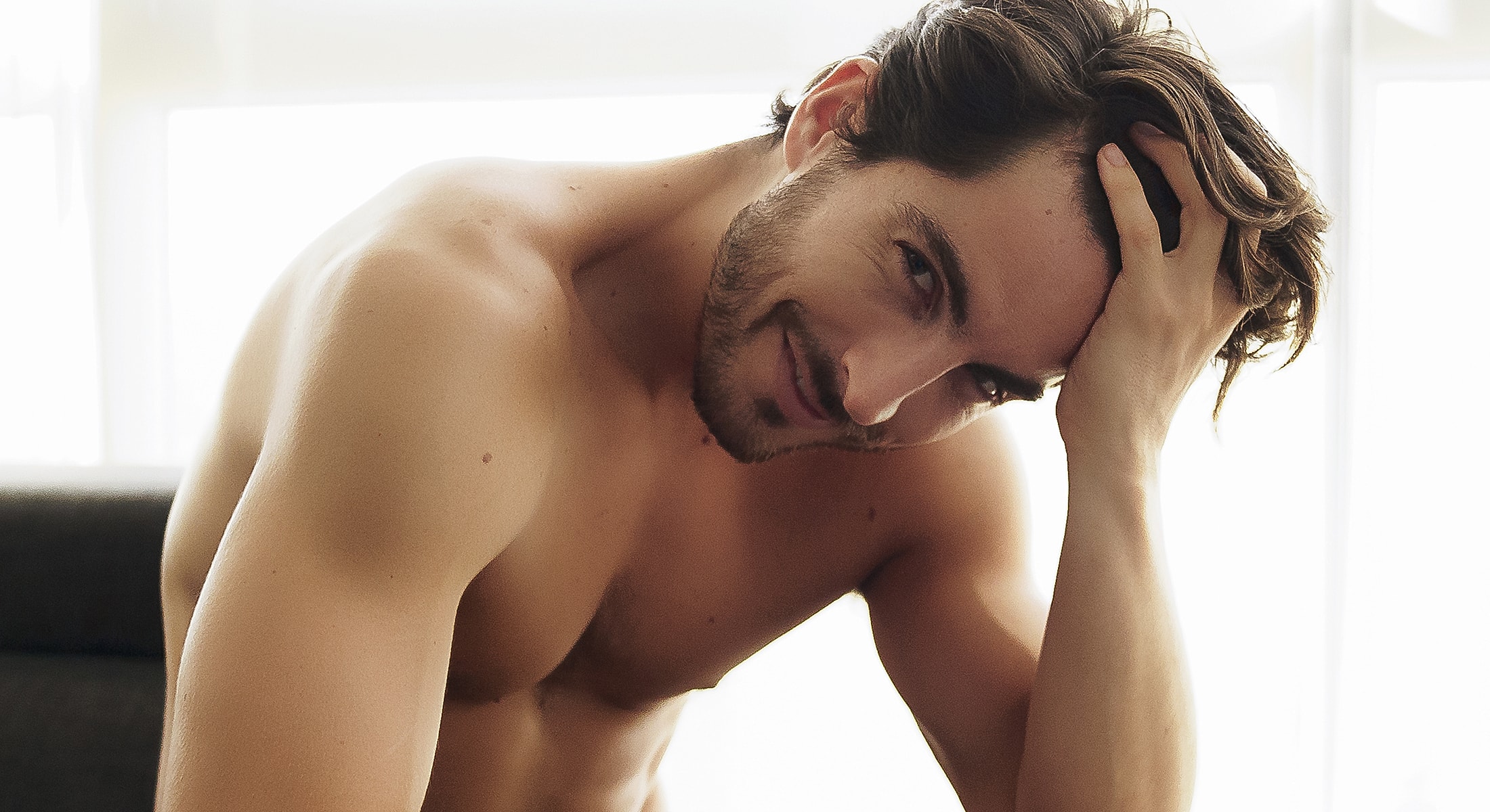 Smiling man with tousled hair in sunlight.