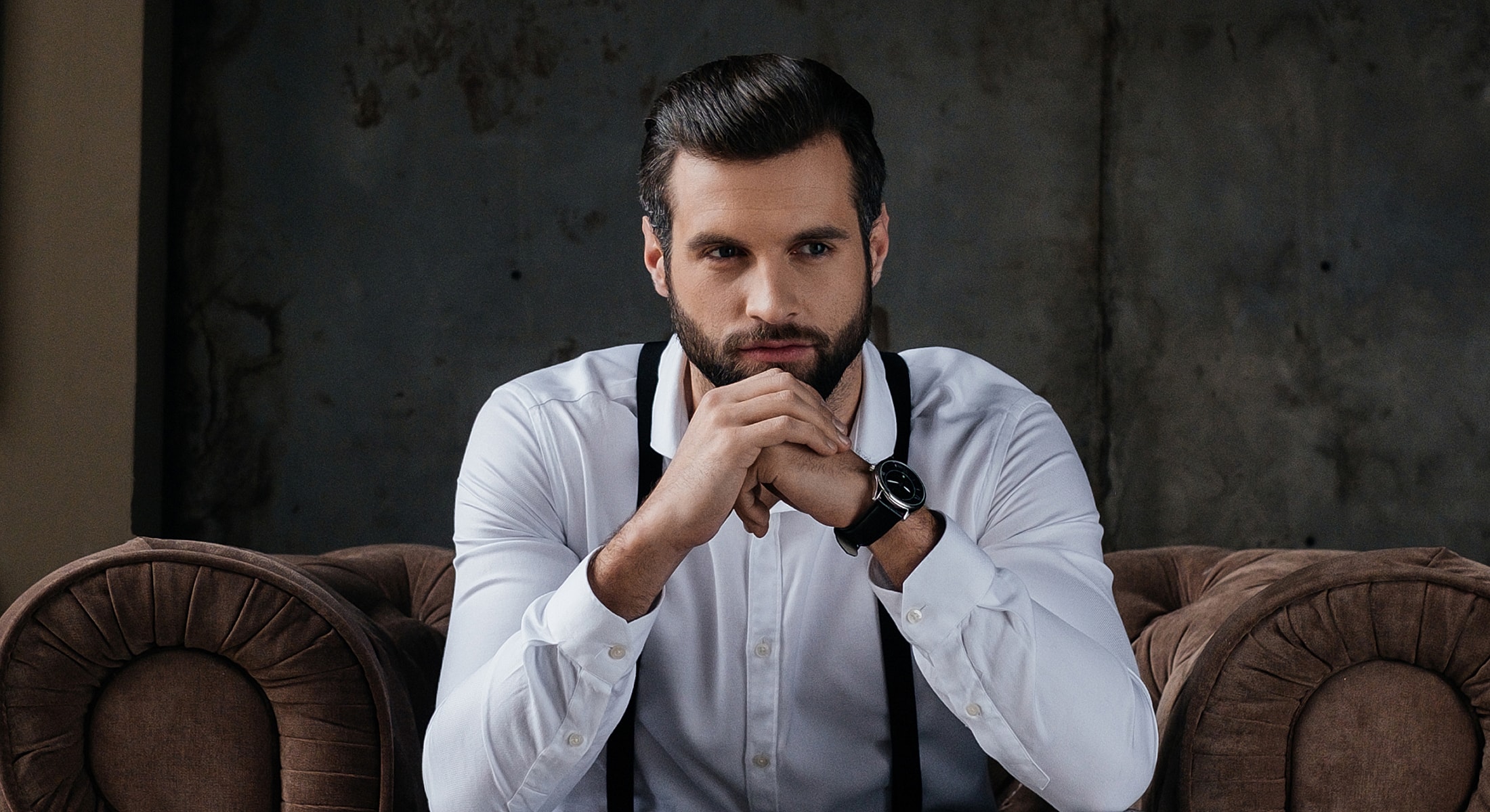 Man in white shirt sitting thoughtfully on couch.