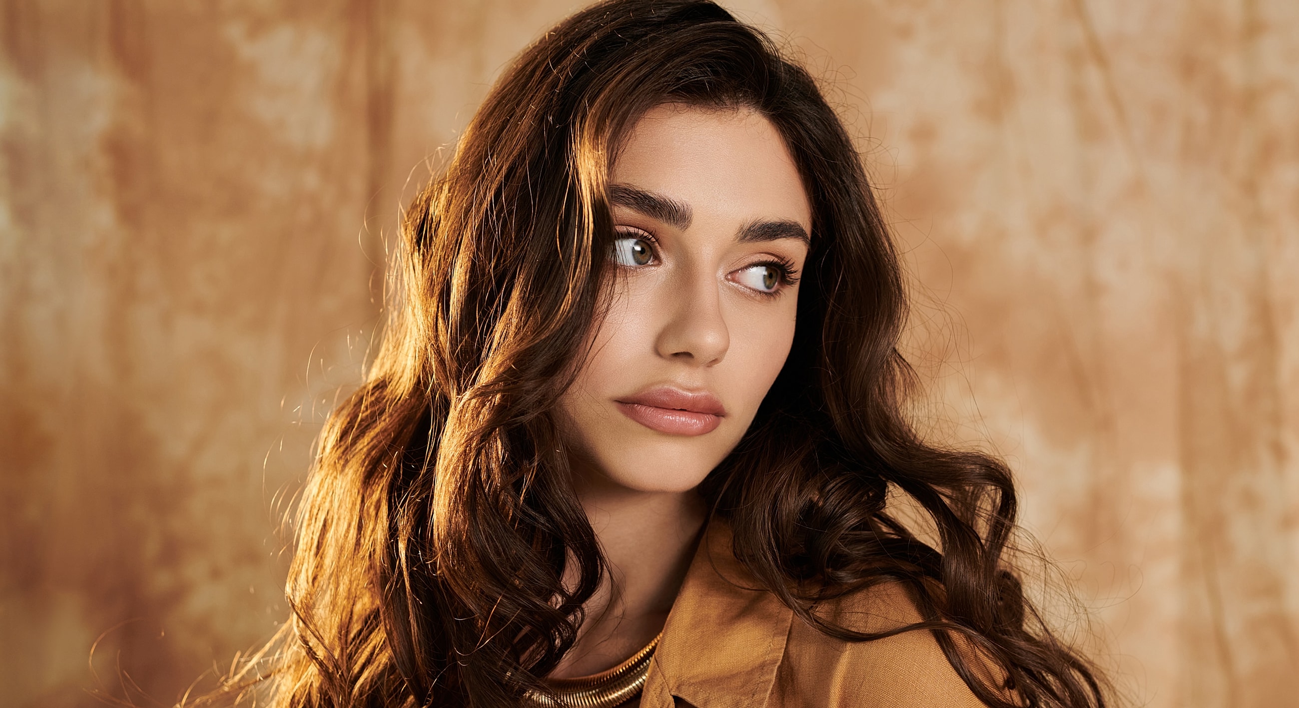 Young woman with wavy hair, neutral background.